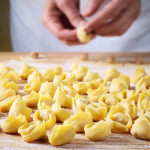 Man`s hands making tortellini on pastry board.