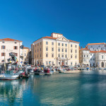 Mediterranean sunny port in slovenia, harbour view city of piran, old mediterranean houses and ships in the bay. Skyline with clocktower in back